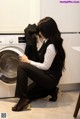 A woman sitting on the floor in front of a washing machine.